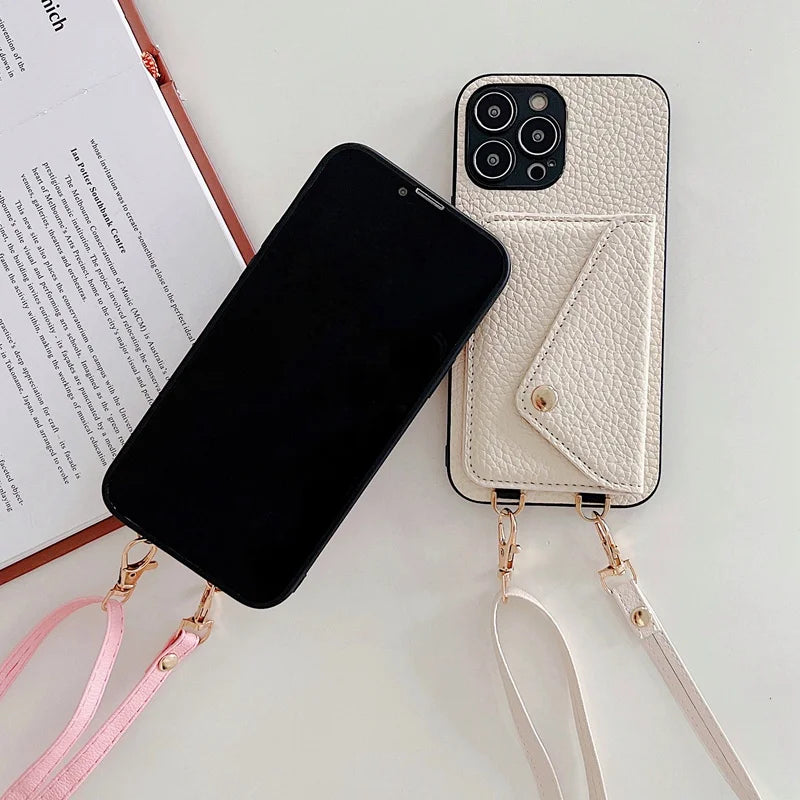 Black phone next to a white leather phone case with strap on a light surface