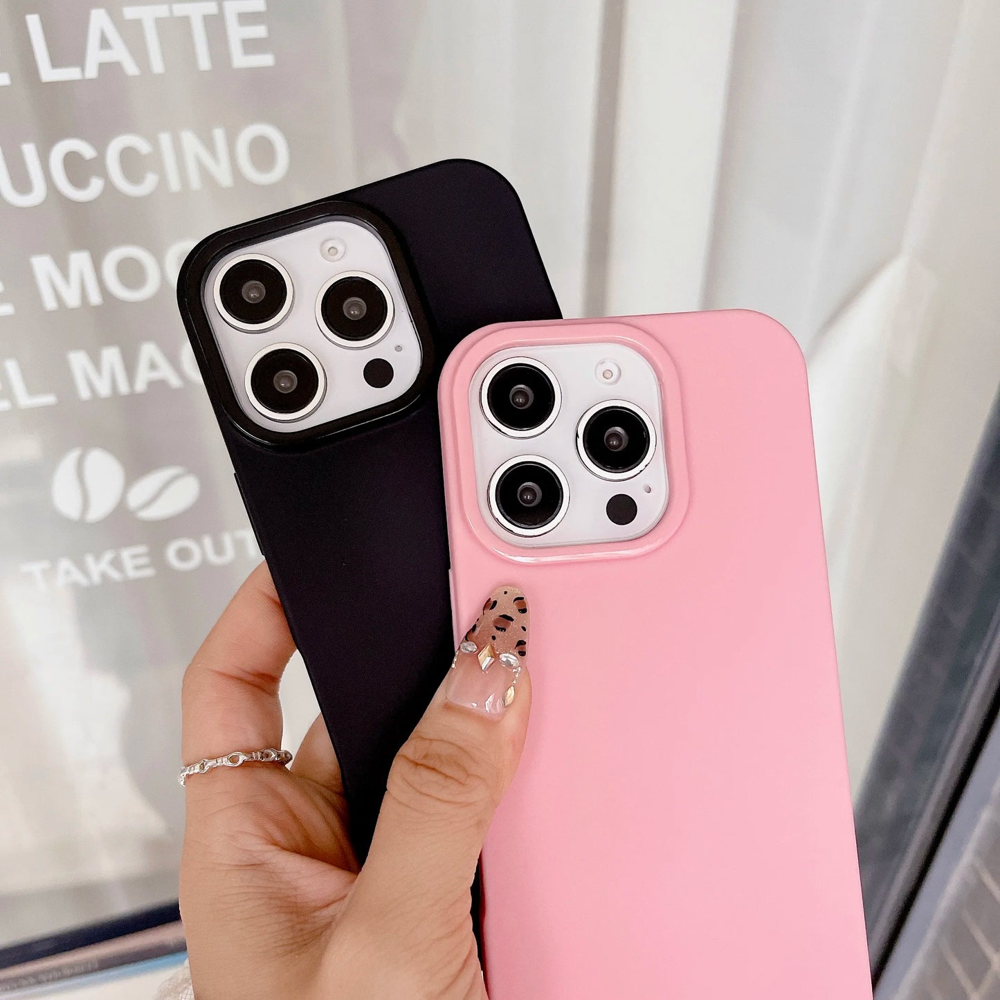 Black and pink phone cases held by a hand with a blurred background
