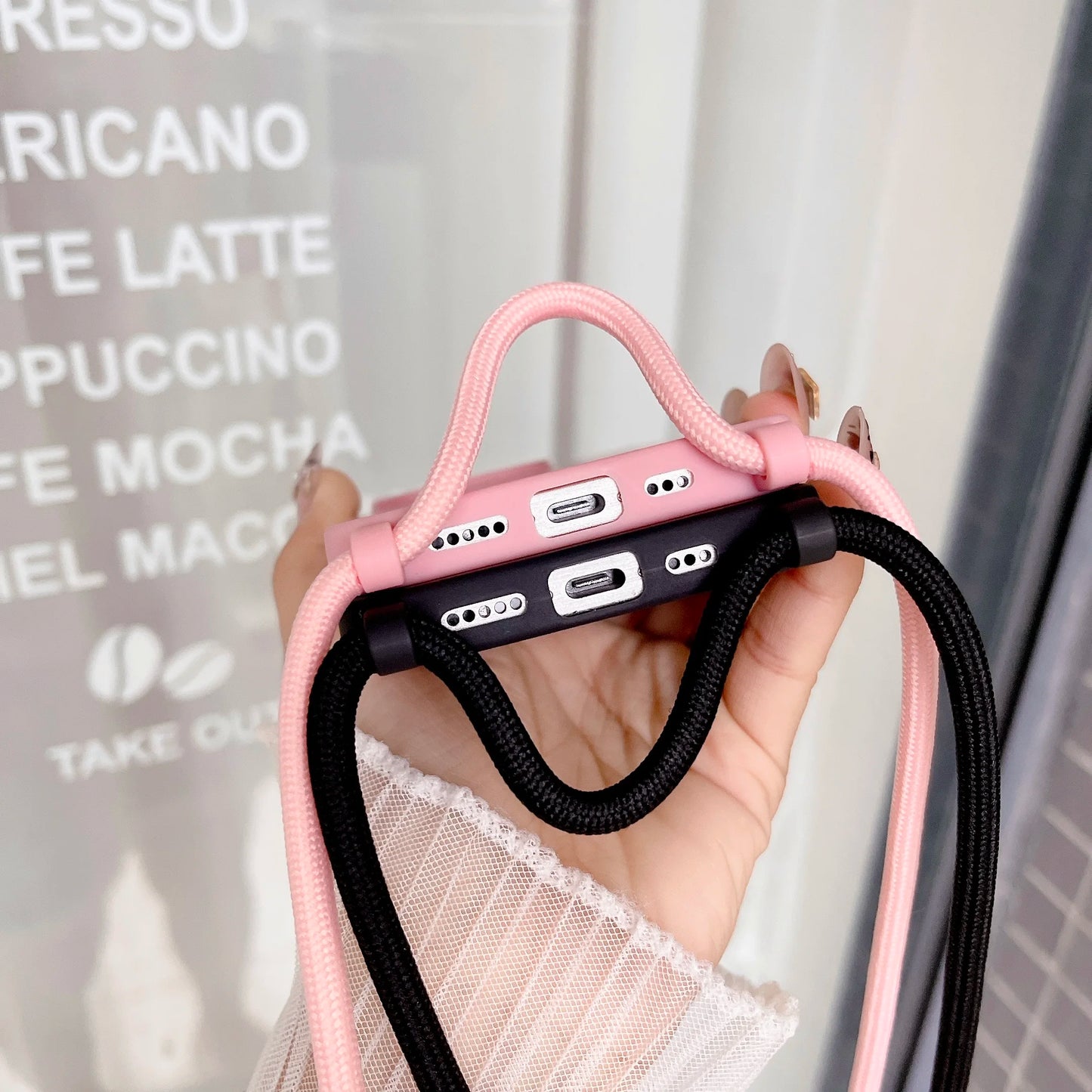 Pink and black phone cases with straps held up by a hand to show the charging port, blurred background
