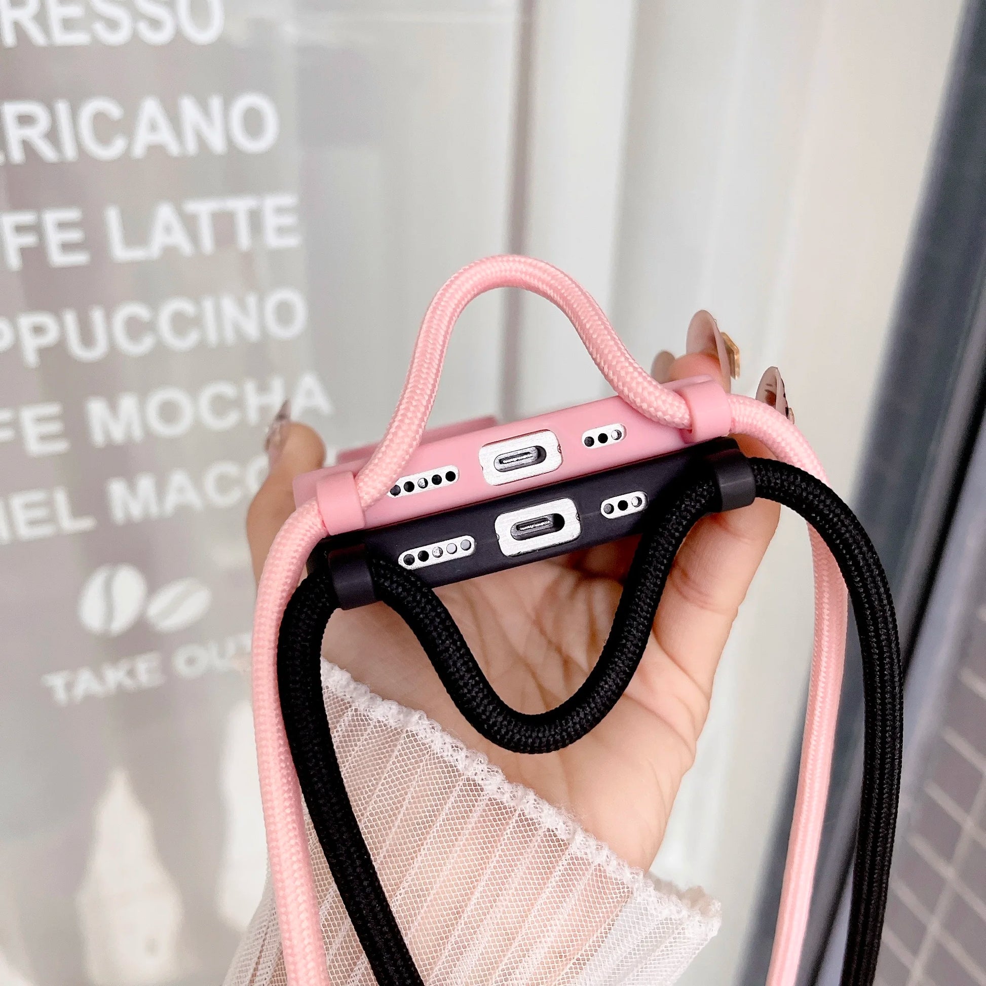 Pink and black phone cases with straps held up by a hand to show the charging port, blurred background
