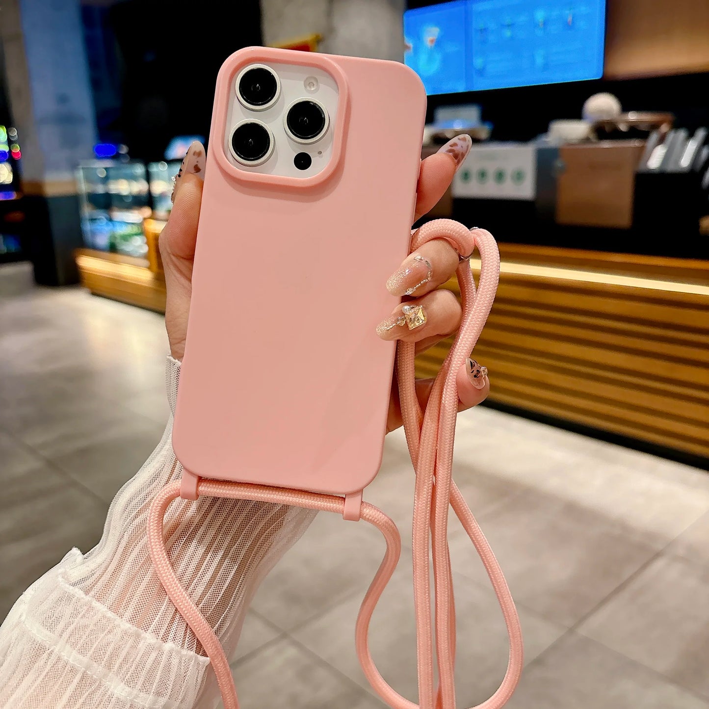 Person holding a pink phone case with a strap in an indoor setting