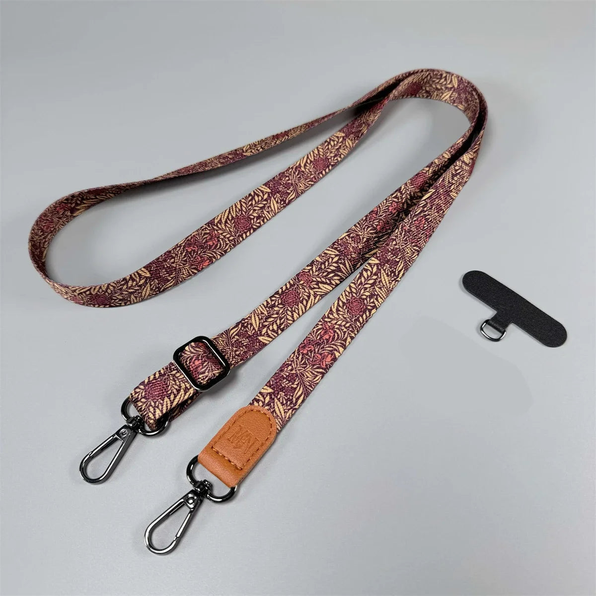 Red/Pink nature print cross body phone lanyard with adjustable strap and leather ends on a grey background. 