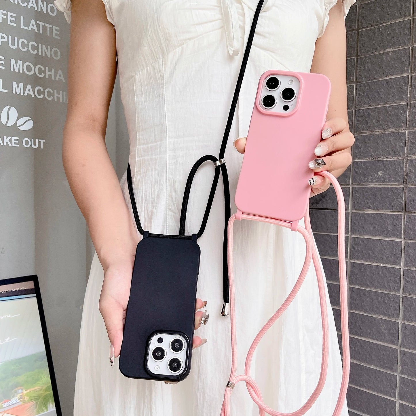 Person holding two phone cases, one pink and one black, with straps.