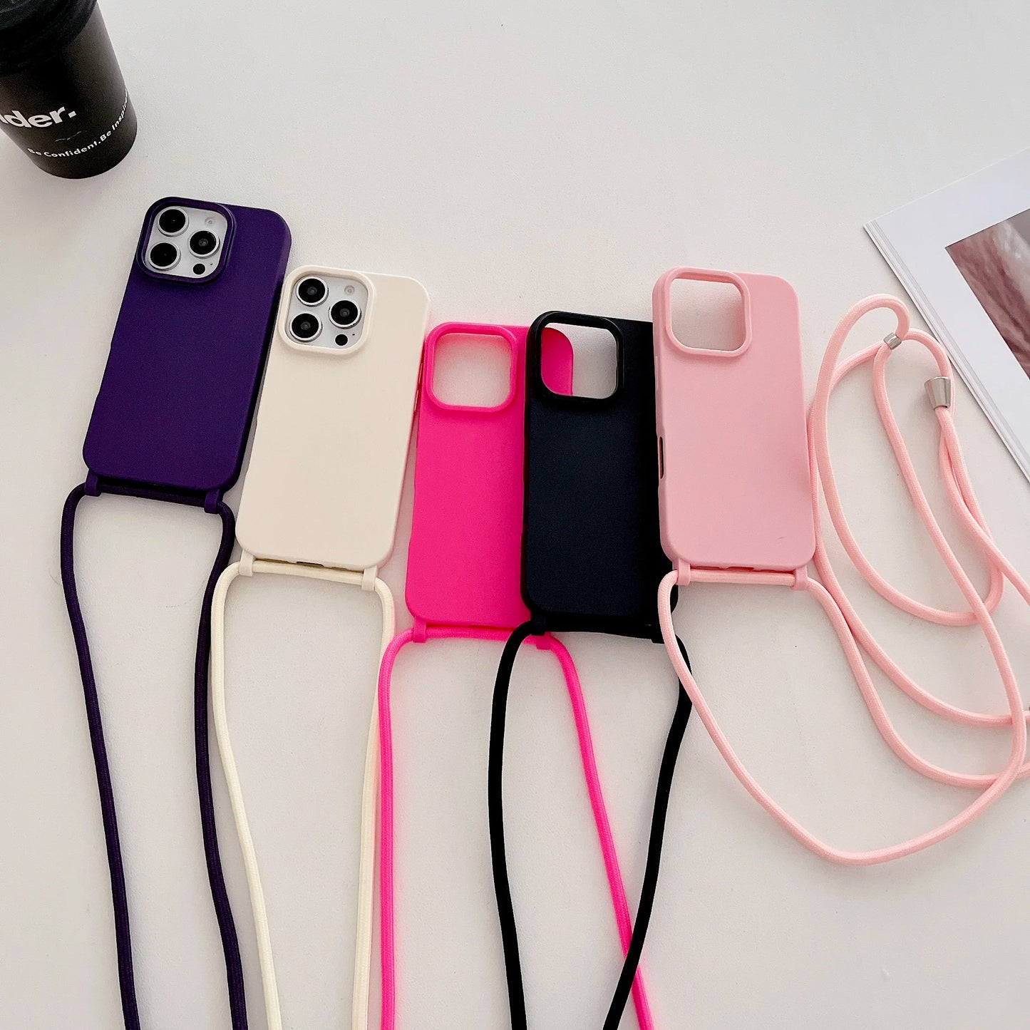 Five phone cases with straps in purple, white, pink, black, and pink on a light background.