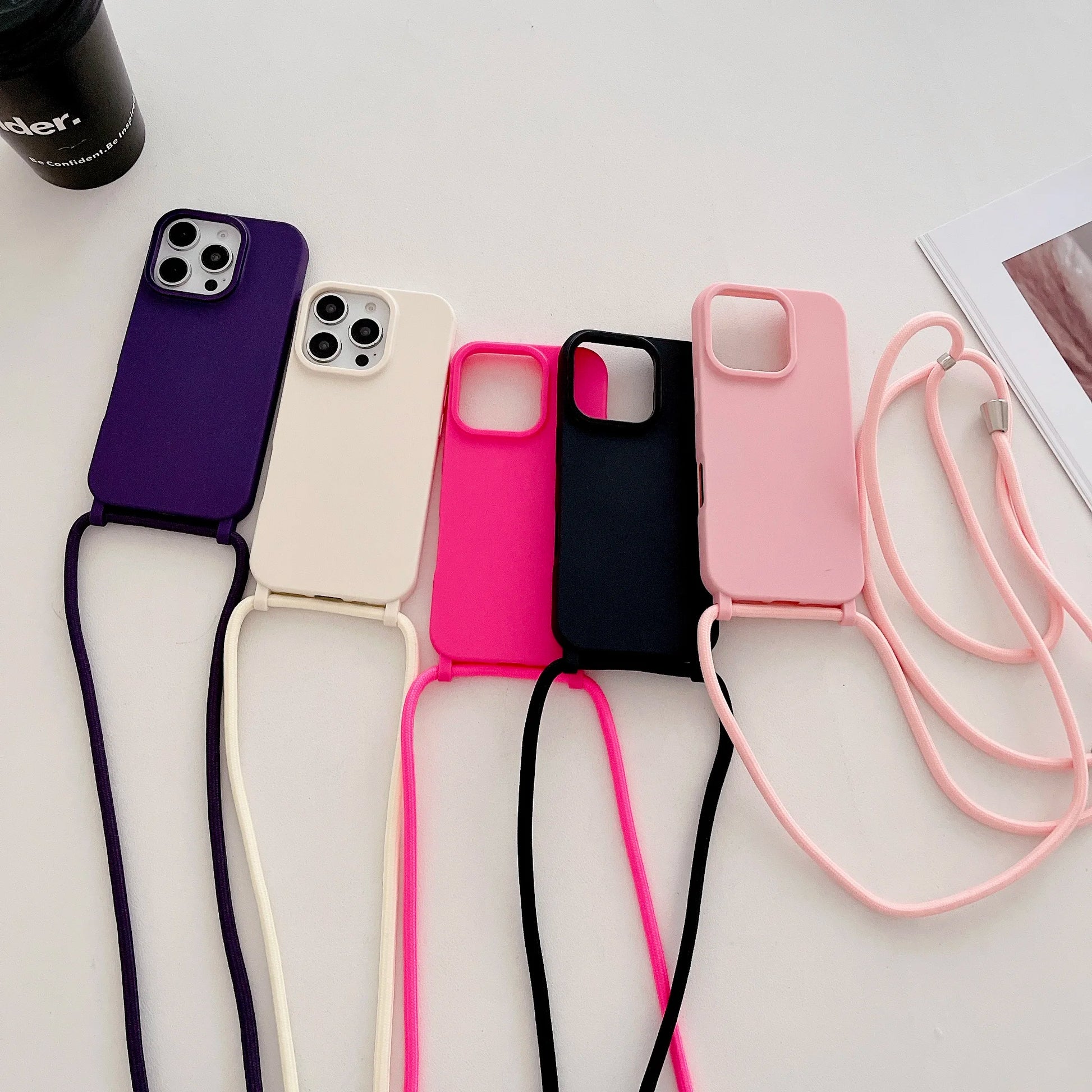 Five phone cases with straps in purple, white, pink, black, and pink on a light background.