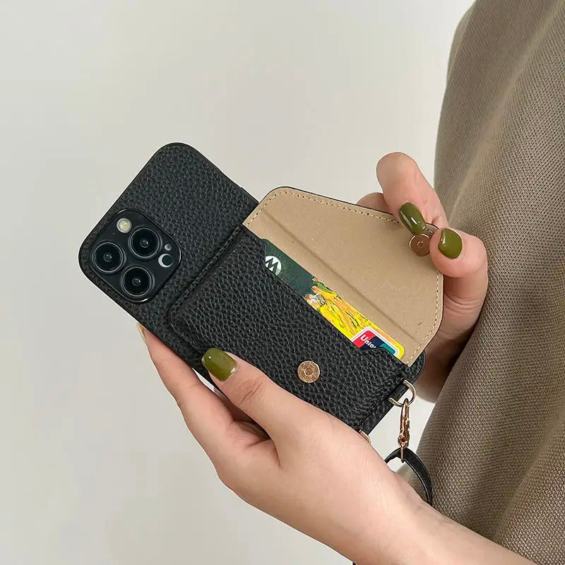 A person holding a black leather phone case with strap demonstrating how the card wallet feature of the case works.
