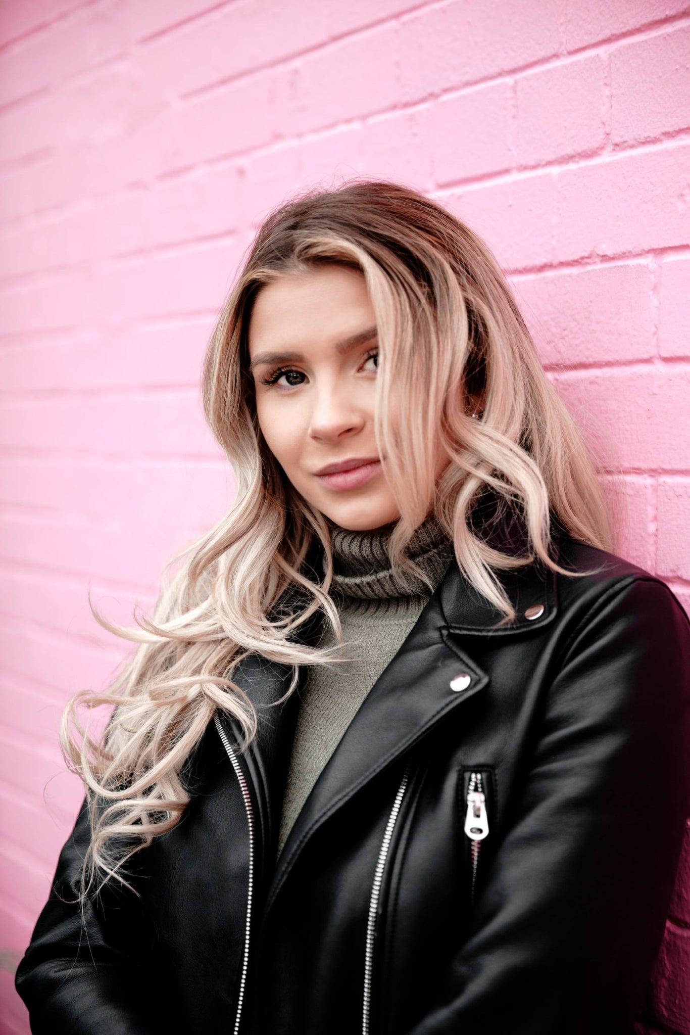 Person wearing a black leather jacket against a pink brick wall